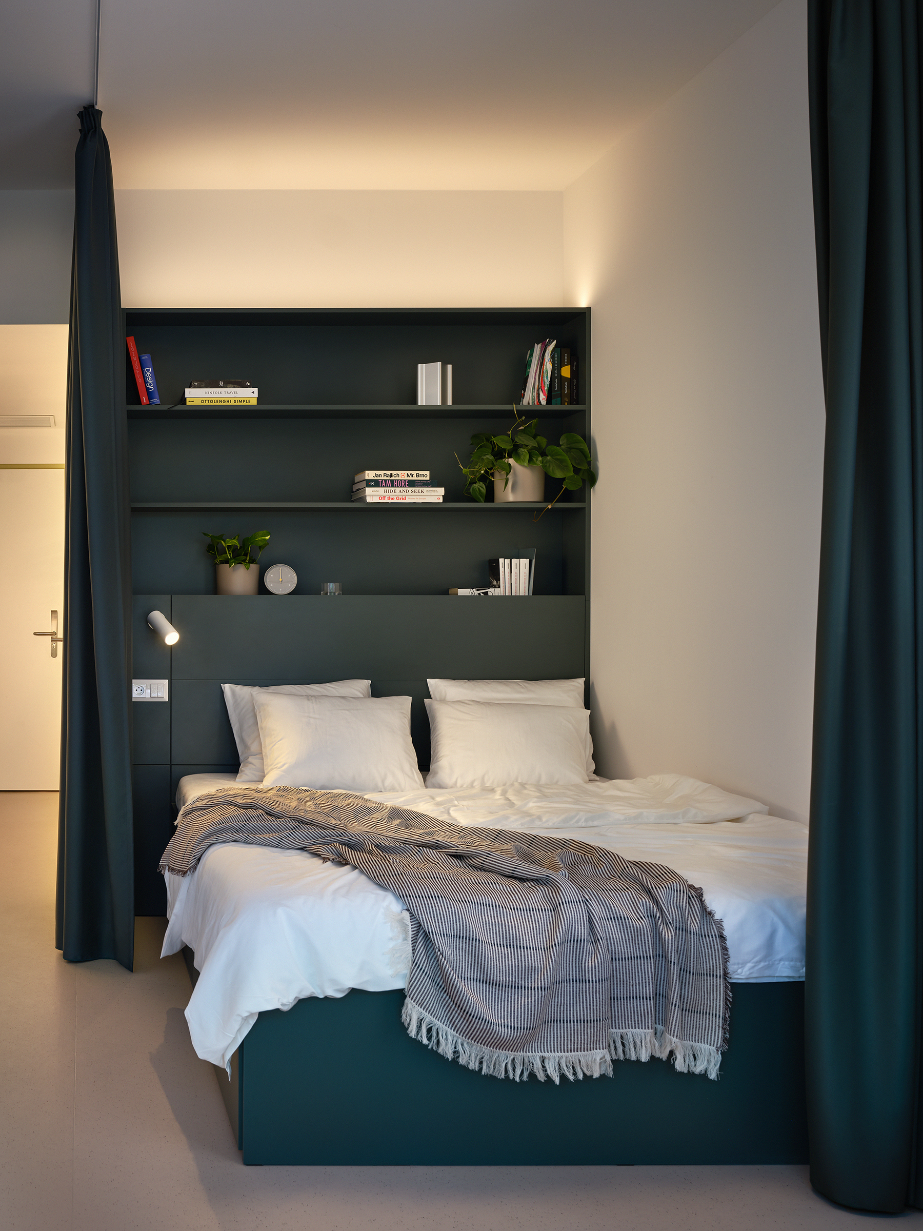 Modern bedroom with a dark teal built-in shelving unit above a bed, white bedding, and a gray striped throw blanket.